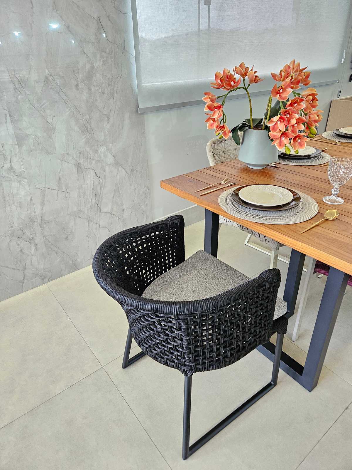 Mesa de jantar posta com cadeira de trama preta em corda náutica e arranjo de flores