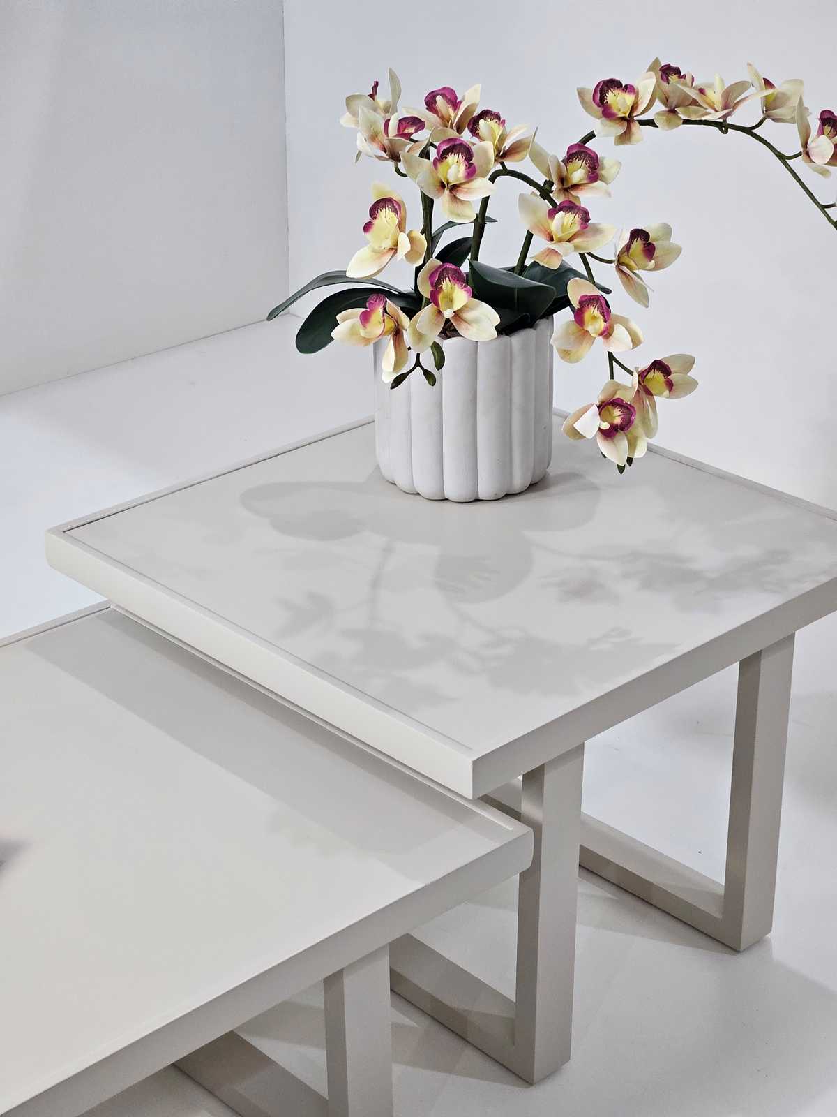 Mesa lateral com tampo claro e vaso canelado com orquídeas