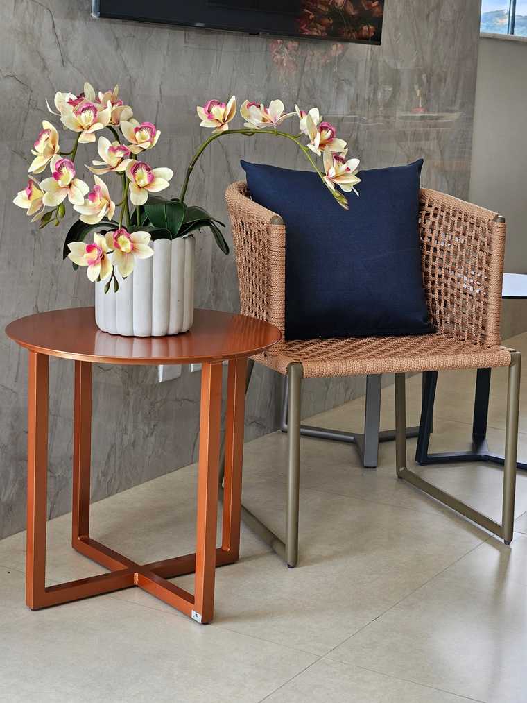 Poltrona de fibra sintética natural com almofada azul, mesa lateral redonda e orquídea