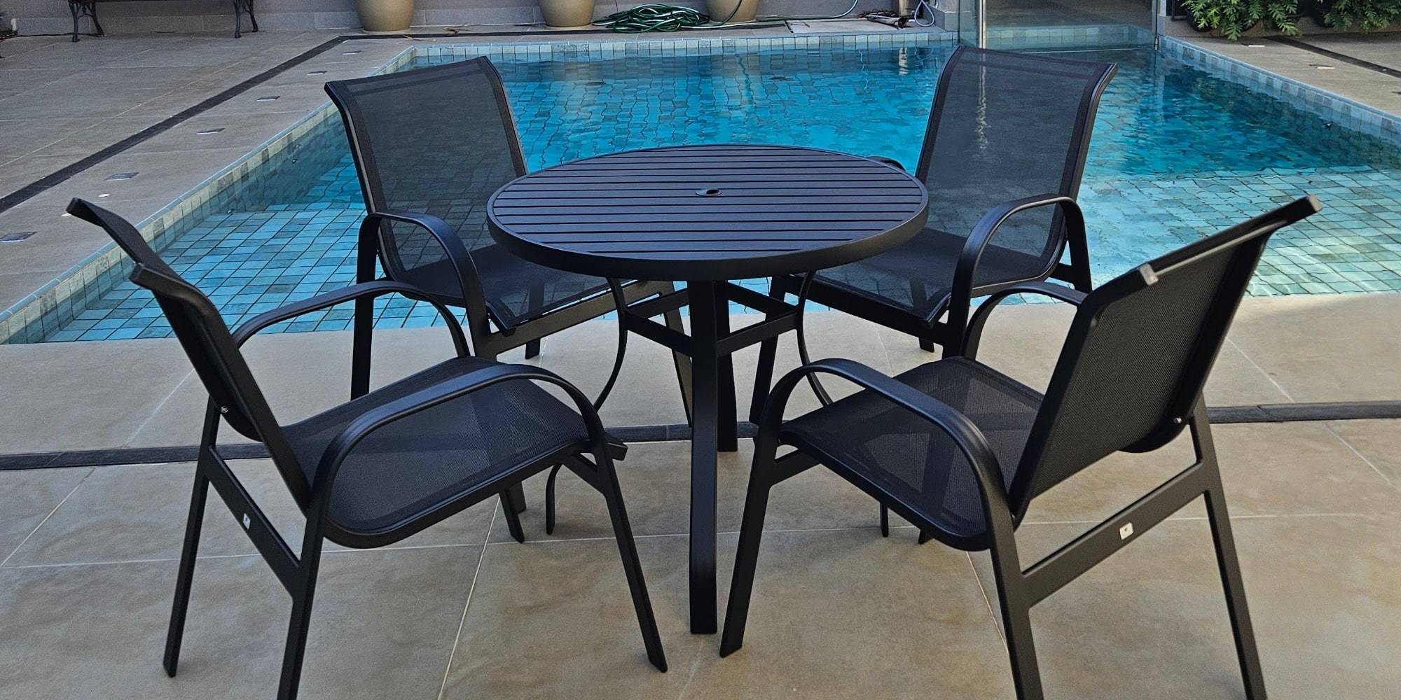 Conjunto de mesa redonda e quatro cadeiras em alumínio posicionado na borda de uma piscina